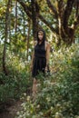 Brooding dreamy young girl blonde, black dress with a hood standing by a tree Royalty Free Stock Photo