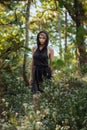 Brooding dreamy young girl blonde, black dress with a hood standing by a tree Royalty Free Stock Photo