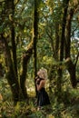 Brooding dreamy young girl blonde, black dress with a hood standing by a tree Royalty Free Stock Photo