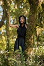 Brooding dreamy young girl blonde, black dress with a hood standing by a tree Royalty Free Stock Photo