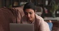 Brooding Indian young woman lying on sofa working on laptop