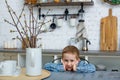 A brooding little blond boy sits at the kitchen table and looks at the camera. Cute little boy gets bored during quarantine. Sad Royalty Free Stock Photo