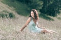 Brooding young woman sitting on the grass of a summer meadow.