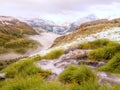 Brook in fresh Alps meadow, snowy peaks of Alps in background. Cold misty and rainy weather in mountains at the end of fall.