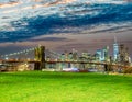 The Brooklyn Bridge at sunset with Manhattan skyline on background and green meadow in foreground, New York City Royalty Free Stock Photo