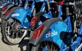 Long row of Citibike corporate sponsored bike share bicycles docked in a dock bay on a street in New York City.