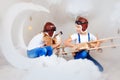 Brother and sister in aviator helmet playing with big wooden airplane in white clouds. Children and their dog together in sky with
