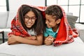 Brother and sister covering with blanket lying on sofa at home