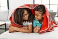 Brother and sister covering with blanket lying on sofa at home