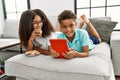 Brother and sister eating cookies using touchpad lying on sofa at home Royalty Free Stock Photo