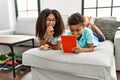 Brother and sister eating cookies using touchpad lying on sofa at home Royalty Free Stock Photo