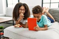 Brother and sister eating cookies using touchpad lying on sofa at home Royalty Free Stock Photo