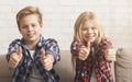 Brother And Sister Gesturing Thumbs-Up Sitting On Couch At Home