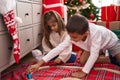 Brother and sister playing with cars sitting on floor by christmas gifts at home