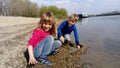 Brother and sister are playing by the river. A boy and a girl are wearing jeans and long-sleeved clothing. Early summer. Smiles