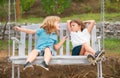 Brother and sister playing in spring park outdoors, swinging in garden wooden swing. Little boy and girl kids enjoying Royalty Free Stock Photo