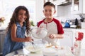 Brother and sister preparing cake mixture together at the kitchen table looking to camera, waist up