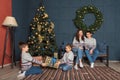 Brother and sister pull a new year present box in the living room with a Christmas tree, and parents in the family look laughing