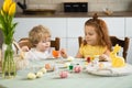 Brother and sister are sitting at the kitchen table and painting Easter eggs. Children getting ready for Easter holidays. Royalty Free Stock Photo