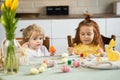 Brother and sister are sitting at the kitchen table and painting Easter eggs. Kids getting ready for Easter holidays.