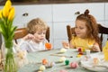 Brother and sister are sitting at the kitchen table and painting Easter eggs. Two kids getting ready for Easter holidays. Royalty Free Stock Photo