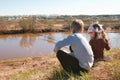 Brother and sister sitting and playing on the riverbank in the village. Back view. Royalty Free Stock Photo