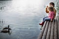 Brother and sister sitting on the river pier and hugging and look at ducks in water. friendship concept. kids feed ducks Royalty Free Stock Photo