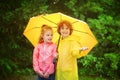 Brother and sister stand together under a big yellow umbrella. Royalty Free Stock Photo