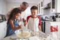 Brother and sister standing at the kitchen table mixing cake mix with their grandfather, close up