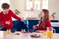 Brother And Sister Wearing School Uniform In Kitchen Have Fun Hanging Spoon From Nose At Breakfast Royalty Free Stock Photo