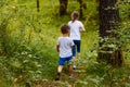 Brother and sister in white t-shirts go into the woods on the path in the summer