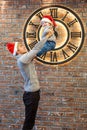 Brother teenager picks up a toddler boy in santa hats indors caps near the huge clock 5 minutes before midnight christmas