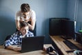 Brothers in the process of distance learning. The younger brother sits at the table and looks at his laptop. The older brother