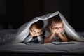 Two kids using tablet pc under blanket at night.