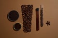 On brown background, lab glassware container coffee beans, grounds and liquid decorated. Shape of cosmetic tube arranged by Royalty Free Stock Photo