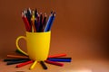 On a brown background on the left is a yellow mug with colored pencils and wax crayons Royalty Free Stock Photo