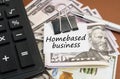 On a brown background lies a calculator and dollars on a clip with an inscription on paper - Homebased business