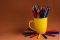 On a brown background on the right is a yellow mug with colored pencils and wax crayons Royalty Free Stock Photo