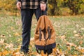 A brown backpack in the hand of a guy in the autumn forest.