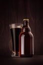 Brown beer bottle belgian steinie and glass pilsner with porter on dark wood board, vertical, mock up. Royalty Free Stock Photo