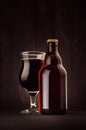 Brown beer bottle and glass tulip with porter on dark wood board, vertical, mock up. Royalty Free Stock Photo