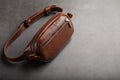 A brown belt bag made of textured brown leather on a black stone background. Elegant fanny pack brown bag with a zipper