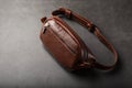 A brown belt bag made of textured brown leather on a black stone background. Elegant fanny pack brown bag with a zipper