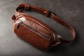 A brown belt bag made of textured brown leather on a black stone background. Elegant fanny pack brown bag with a zipper