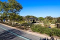 A brown and black pergola in the garden surrounded by a dirt path and lush green trees and plants