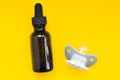 Brown bottle of vitamin d and grey soother on yellow background. Concept of daily receiving vitamins, baby health.