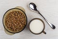 Brown bowl with boiled buckwheat, spoon, cup of milk