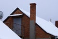 Brown brick long chimney pipe on the roof in white snow