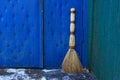 A brown broom stands at the blue door and the green wall outside in the snow