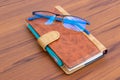 Brown business diary with ball pen and specks lying on wooden table Royalty Free Stock Photo